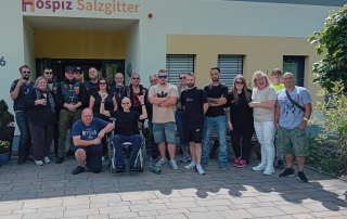 19 Männer und Frauen (Biker), inklusiv Gast im Rollstuhl, stehen vor Hospizeingang