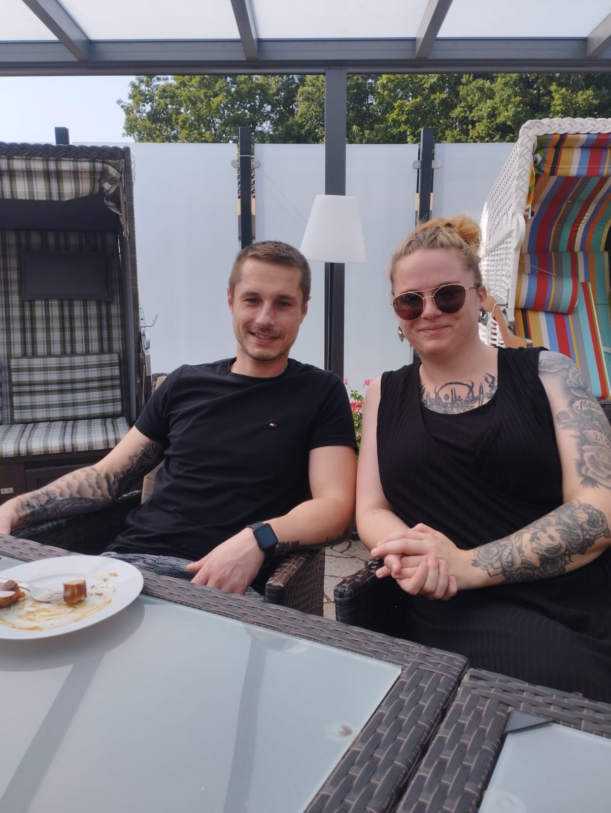 Eine junge Frau und ein junger Mann sitzen am Tisch und schauen freundlich in die Kamera Eine junge Frau und ein junger Mann sitzen am Tisch und schauen freundlich in die Kamera