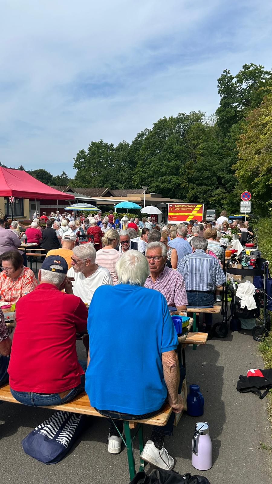 Auf dem Hospizparkplatz stehen viele Bierzeltgarnituren und Menschen sitzen darauf und essen