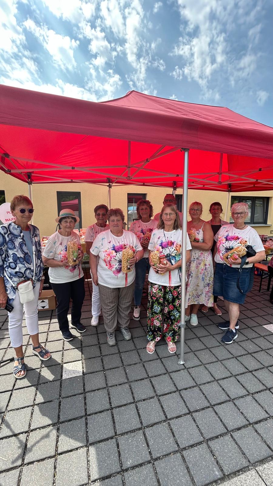 Eine ehrenamtliche Mitarbeiterin und eine Mitarbeiterin vom Sozialdienst stehen mit den Siegern (Kreativgruppe der Wohnbau Salzgitter) ihres schönsten Tisches beim Bürger Brunch unter Pavillon vor dem Hospiz