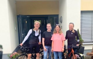 Mann mit Fahrrad, Frau mit Fahrrad und 2 Mitarbeiter vom Hospiz stehen vor Hospiz-Eingangstür