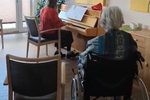 Frau spielt Klavier und Gast im Rollstuhl hört zu