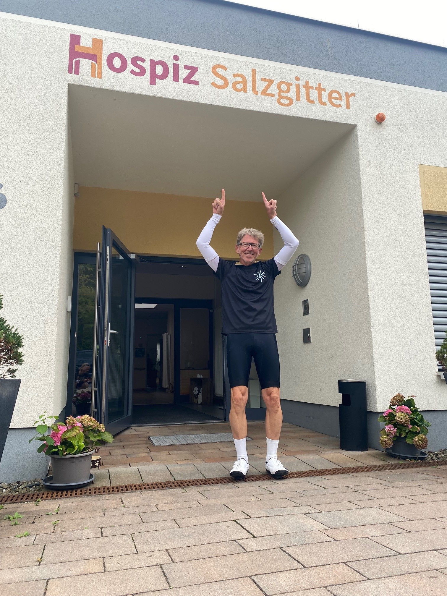 Mann steht vor Hospiz-Eingangstür und zeigt mit Fingern auf den Schriftzug Hospiz Salzgitter