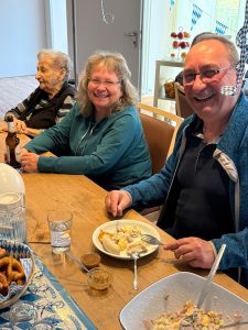 Angehörige vom Gast und Gast sitzen am Tisch, schauen fröhlich und essen