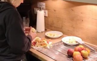 Pflegekraft steht in der Küche und schält Äpfel