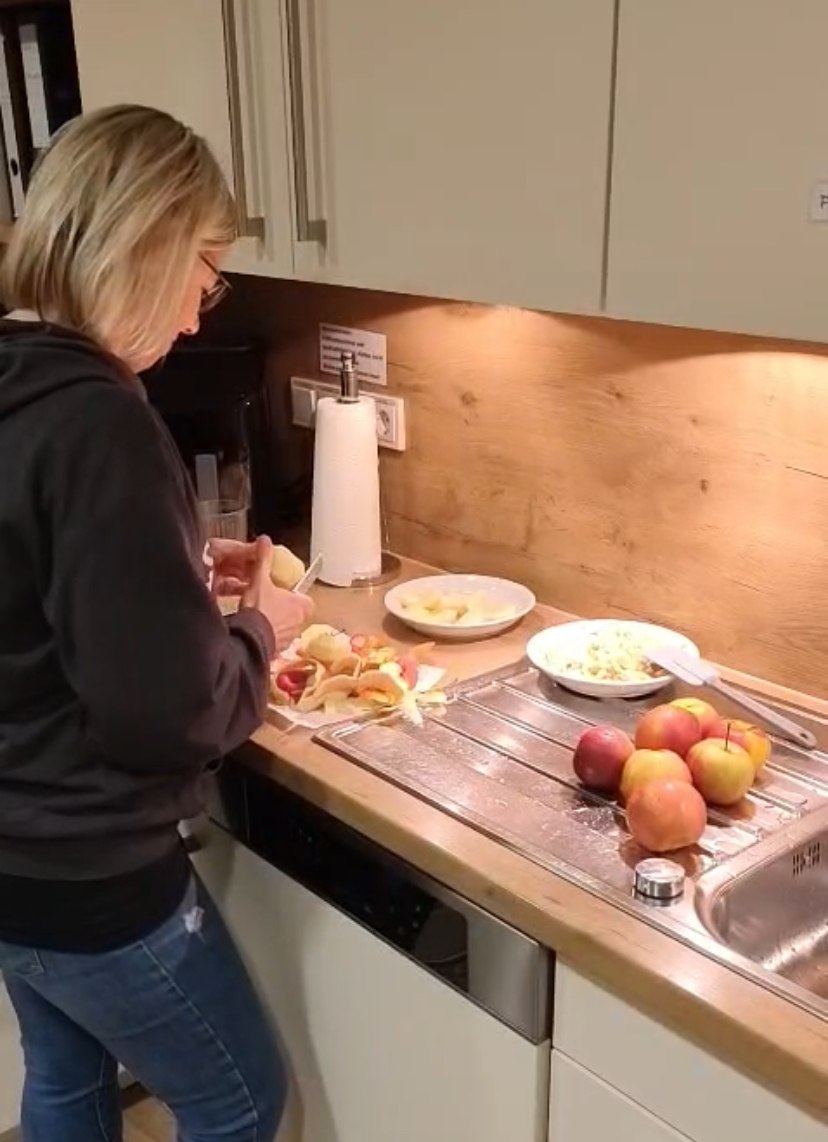 Pflegekraft steht in der Küche und schält Äpfel