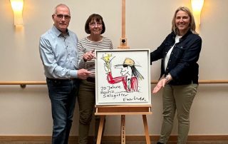 Ein Mann und zwei Frauen stehen neben einem Bild