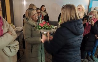 Frau übergibt einer anderen Frau einen Blumenstrauß