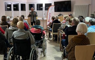 Mehrere Menschen sitzen in einem Raum und hören sich einen Vortrag an