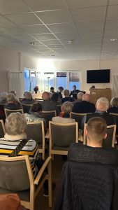 Mehrere Menschen sitzen auf Stühlen und hören den Musikern mit dem Akkordeon zu