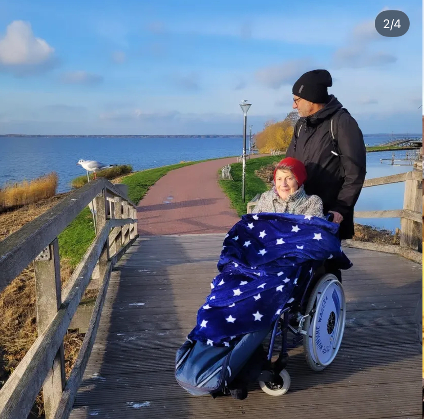 Ein Mann und eine Frau im Rollstuhl stehen auf einer Brücke am Meer