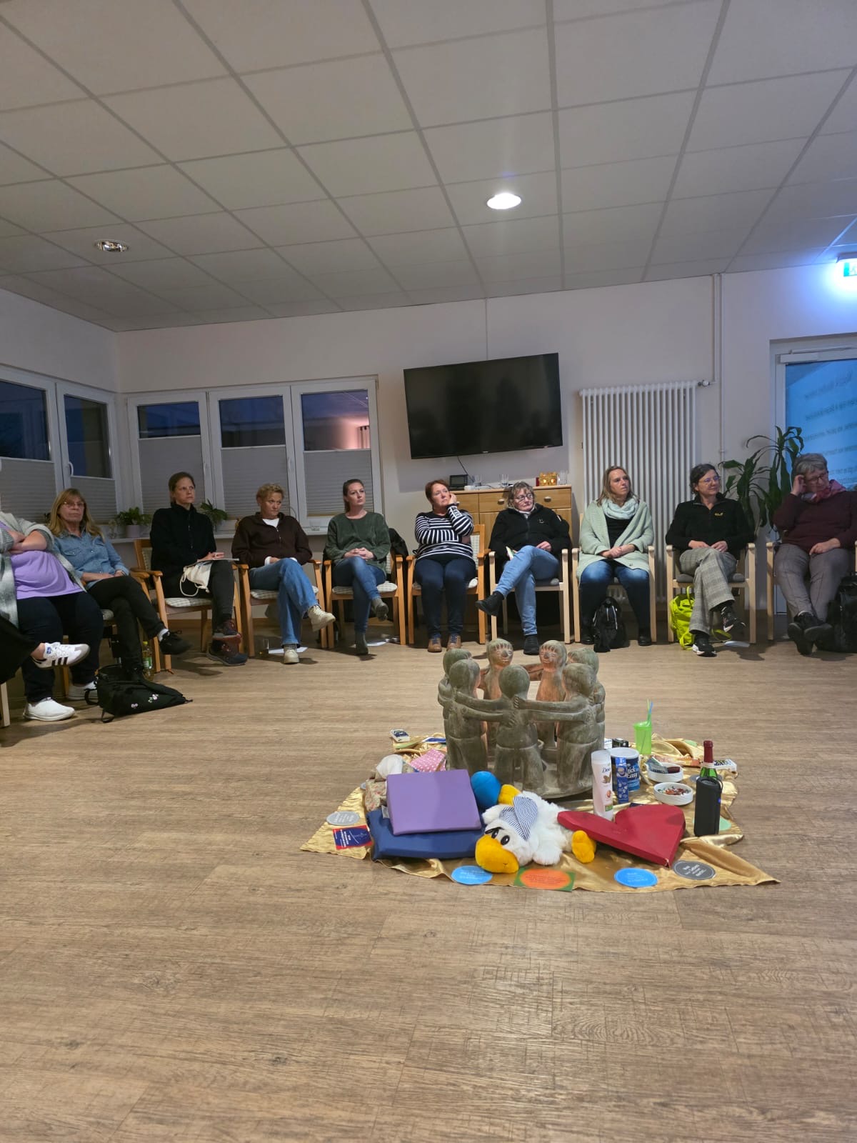 Mehrere Menschen sitzen in einem Kreis. In der Mitte stehen mehrere Gegenstände für den Vortrag Letzte-Hilfe-Kurs Mehrere Menschen sitzen in einem Kreis. In der Mitte stehen mehrere Gegenstände für den Vortrag Letzte-Hilfe-Kurs