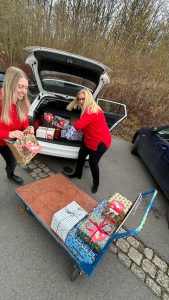 2 Frauen packen Weihnachtsgeschenke aus einem Kofferraum auf einen Wagen