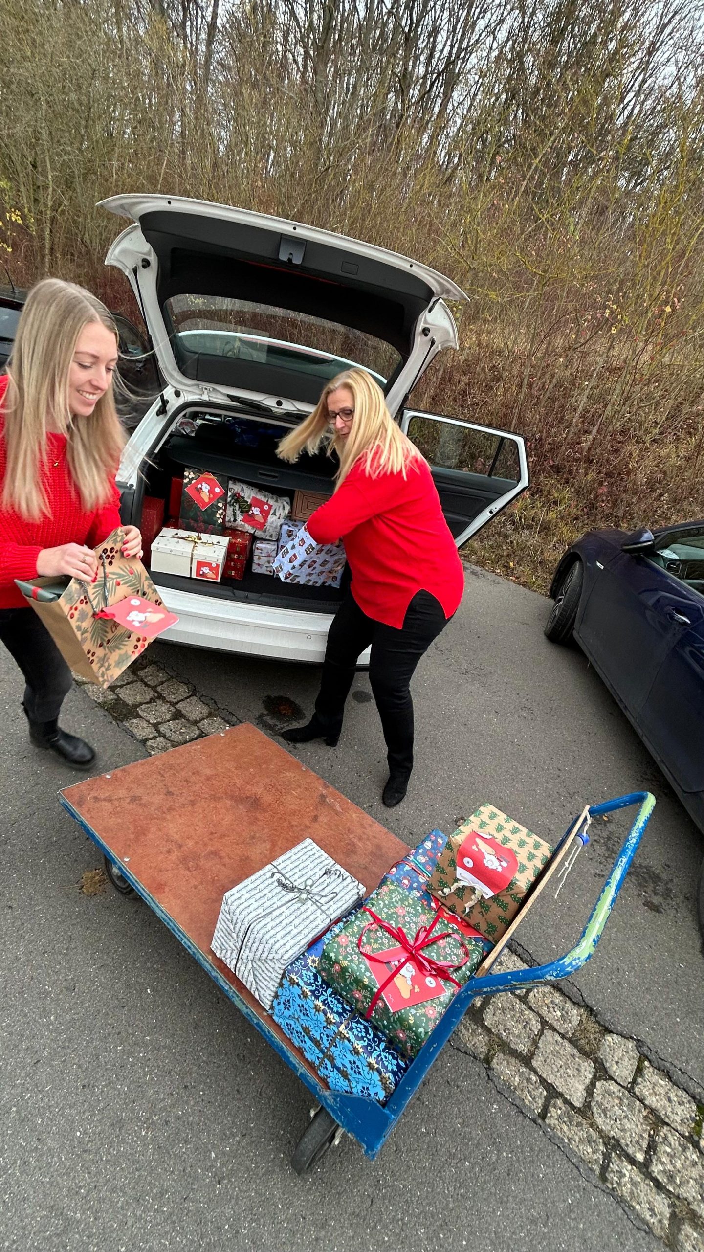 2 Frauen packen Weihnachtsgeschenke aus einem Kofferraum auf einen Wagen 2 Frauen packen Weihnachtsgeschenke aus einem Kofferraum auf einen Wagen