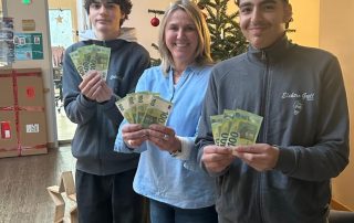 Eine Frau und zwei Jugendliche stehen vor einem Weihnachtsbaum und halten Geldscheine in den Händen