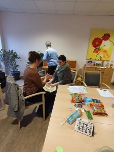 Zwei Frauen sitzen sich gegenüber. Auf den Knien liegt ein Handtuch. Über dem Handtuch sind die Hände der beiden Frauen