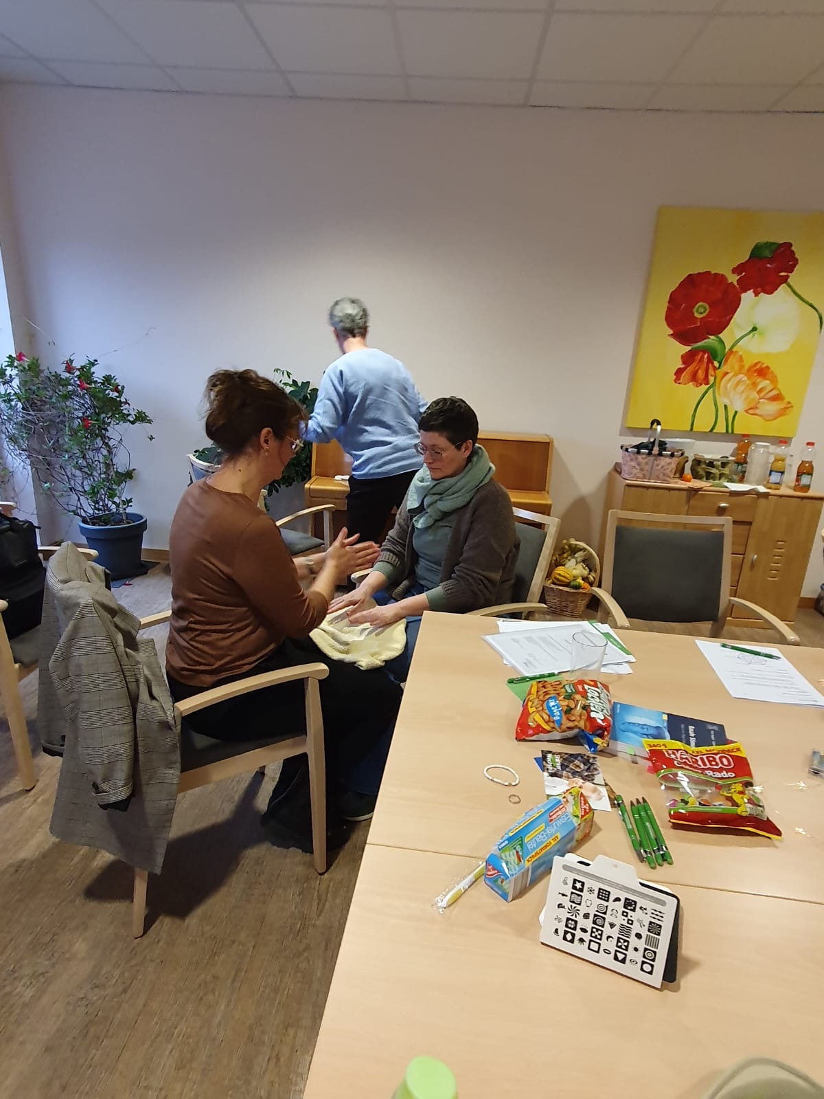 Zwei Frauen sitzen sich gegenüber. Auf den Knien liegt ein Handtuch. Über dem Handtuch sind die Hände der beiden Frauen Zwei Frauen sitzen sich gegenüber. Auf den Knien liegt ein Handtuch. Über dem Handtuch sind die Hände der beiden Frauen