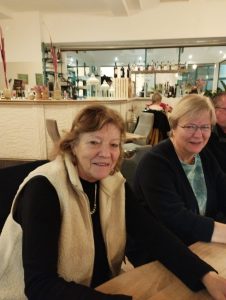 Zwei Frauen sitzen am Tisch und lächeln in die Kamera