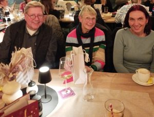 Ein Mann und zwei Frauen sitzen am Tisch und auf dem Tisch stehen Weihnachtstüten