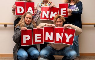 5 Frauen stehen zusammen und halten einen Schriftzug DANKE PENNY in den Händen. Vor Ihnen liegen Süßigkeiten