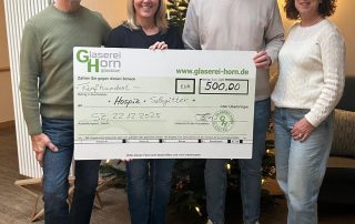 Zwei Frauen und zwei Männer stehen mit einem großen Scheck in der Hand vor einem Weihnachtsbaum