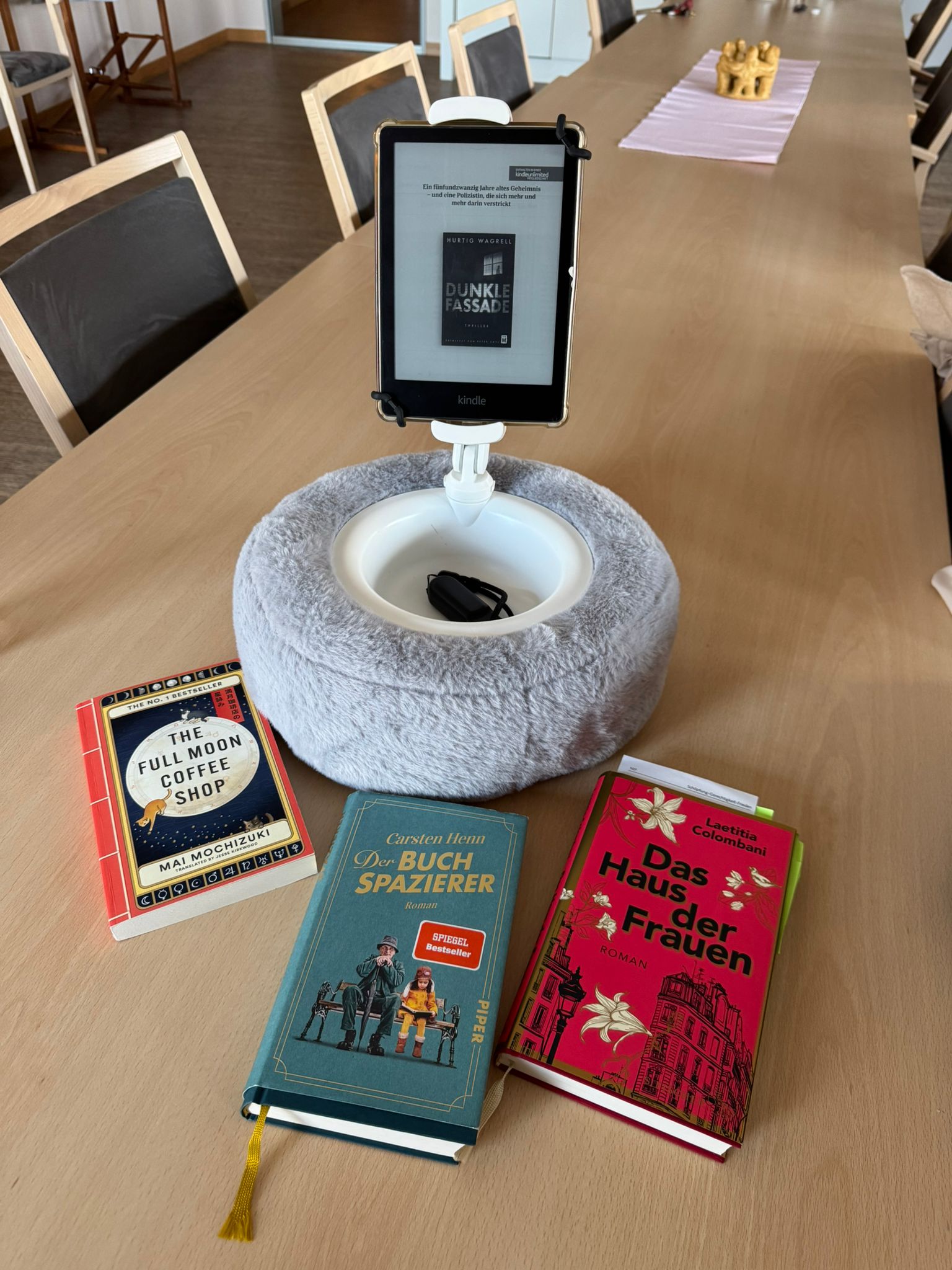 3 Bücher und ein E-Book-Reader in einer Halterung liegen bzw. stehen auf einem Tisch