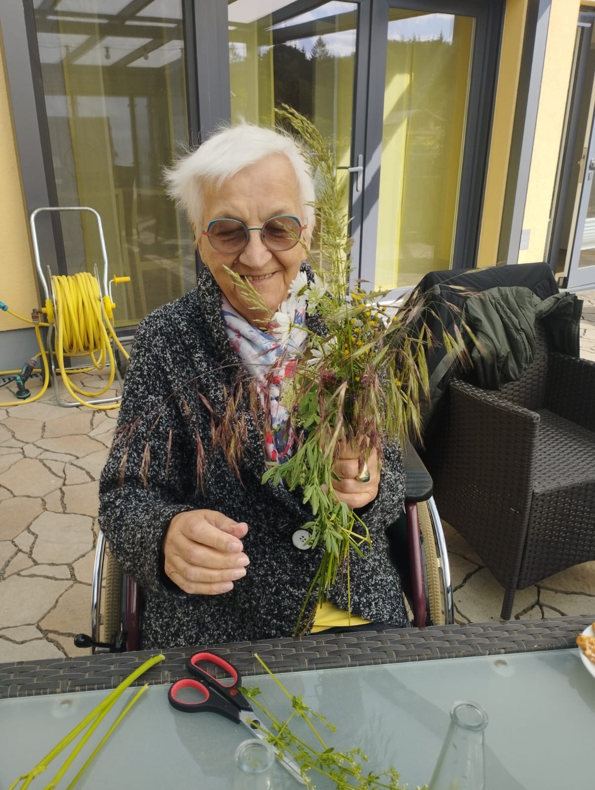 Gast sitzt im Rollstuhl auf der Terrasse und gestaltet einen Blumenstrauß Gast sitzt im Rollstuhl auf der Terrasse und gestaltet einen Blumenstrauß