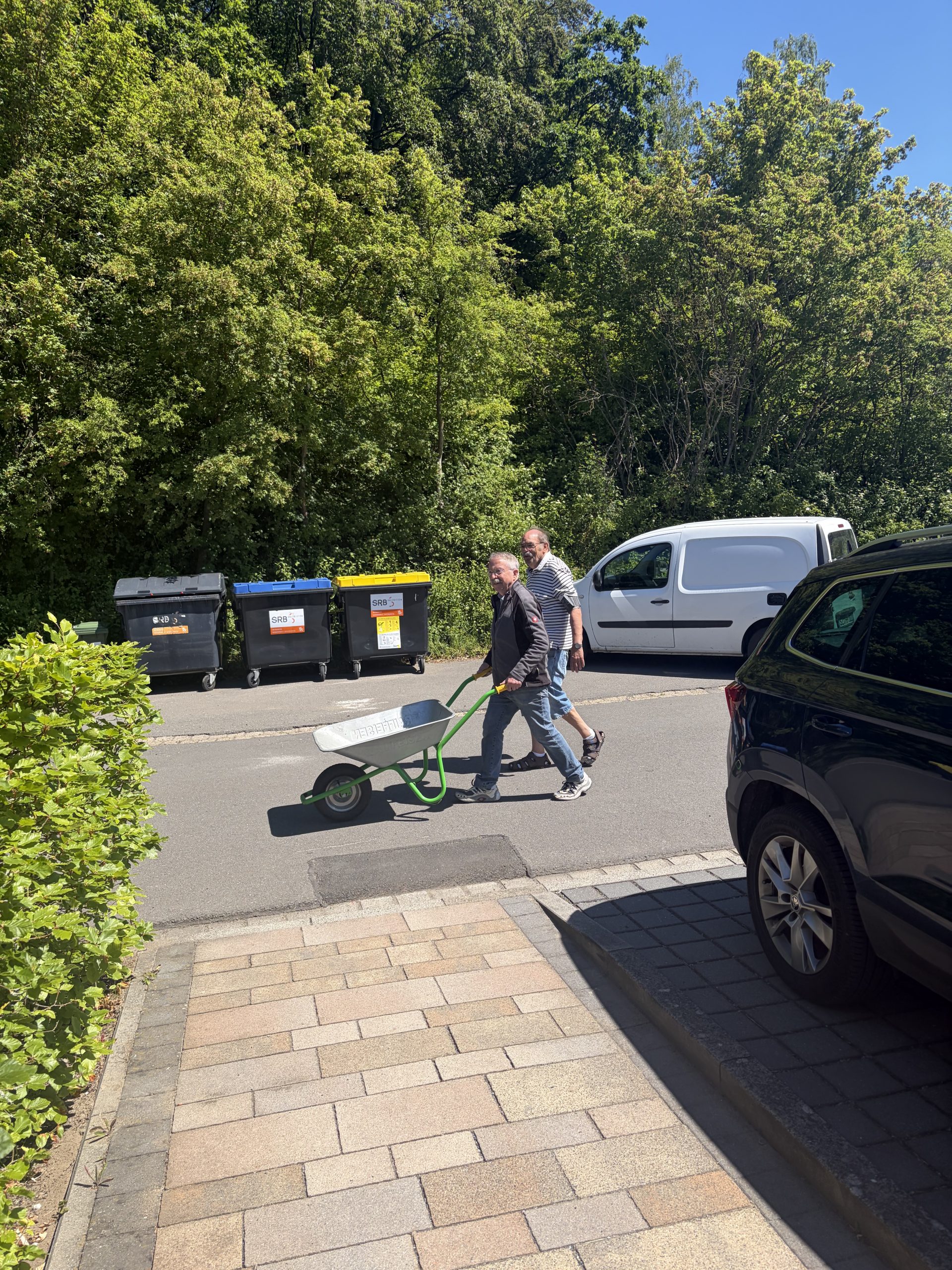 Ehrenamtlicher Hausmeister Ralf Kielkowsky schiebt eine Schubkarre und ehrenamtlicher Hausmeister Paul Piela geht nebenher Ehrenamtlicher Hausmeister Ralf Kielkowsky schiebt eine Schubkarre und ehrenamtlicher Hausmeister Paul Piela geht nebenher
