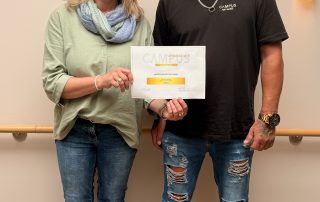Geschäftsführerin Britta Bötel und Oliver Reiter vom Campus am Harz stehen im Hospizeingang mit einem Spendenscheck in der Hand
