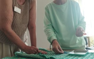 Ehrenamtliche Mitarbeiterin Karin Krökel und Gast stehen in der Küche am Tisch. Auf dem Tisch liegt eine Jacke