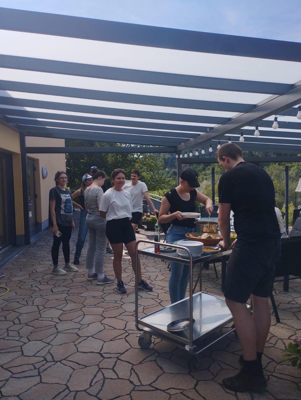 Mitarbeiter von PowerCo stehen auf der Hospiz-Terrasse und füllen sich Suppe in Teller Mitarbeiter von PowerCo stehen auf der Hospiz-Terrasse und füllen sich Suppe in Teller