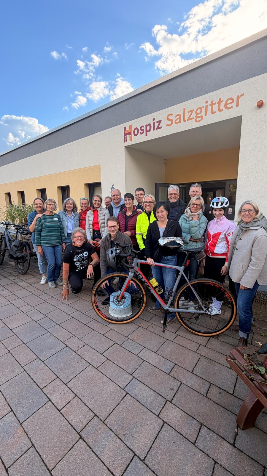 Männer und Frauen stehen mit einem Fahrrad vor dem Hospizeingang