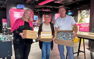 2 Mitarbeiter von der Telekom und Jasmin Libich halten Kartons mit Kronkorken in den Händen