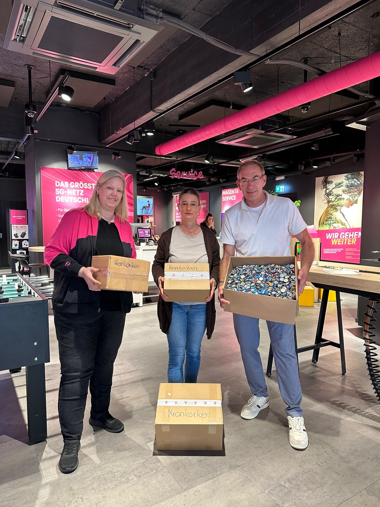 2 Mitarbeiter von der Telekom und Jasmin Libich halten Kartons mit Kronkorken in den Händen